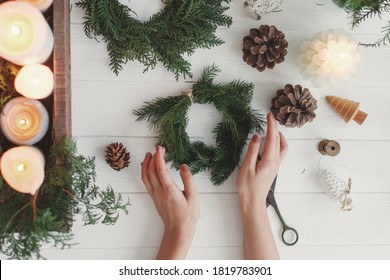 Rustic christmas wreath with candles, pine cones, scissors and ornaments on white wooden table, flat lay. Female hands making simple stylish christmas wreath with fir branches, holiday advent - Powered by Shutterstock