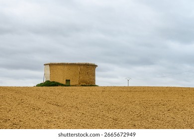 Rustic circular dovecote made of adobe and mud-brick, standing alone on a freshly plowed field near Robladillo de Ucieza
