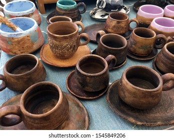 Rustic Clay Cups On An Embroidered White Tablecloth. Rustic Handmade Ceramic Clay Brown Terracotta Cups Souvenirs At The Pottery Studio. Empty Clay Cups. Handmade Kitchenware From Natural Material