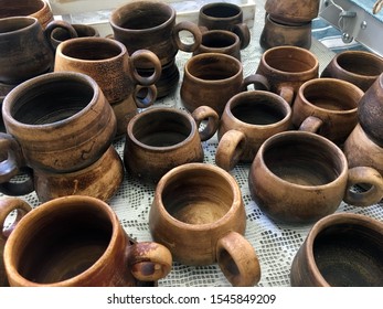 Rustic Clay Cups On An Embroidered White Tablecloth. Rustic Handmade Ceramic Clay Brown Terracotta Cups Souvenirs At The Pottery Studio. Empty Clay Cups. Handmade Kitchenware From Natural Material