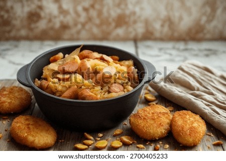 A rustic, close-up view of a black pot filled with a savory sausage and rice mixture, accompanied by golden-brown patties and scattered nuts.