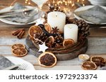 Rustic decor for christmas family dinner. Center piece with white candle, dry orange, cone, cotton. Zero waste eco-friendly home decoration. Cozy atmosphere, wooden background. Close up