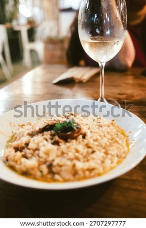 A rustic dining setting featuring a creamy risotto paired with a glass of white wine on a wooden table.