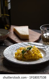 Rustic dinner. Risotto Milanese(saffron risotto) in white plate with glass of white wine and parmesan on wooden table.