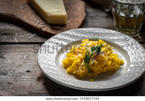Rustic\
dinner. Risotto Milanese(saffron risotto) in white plate with glass\
of white wine and parmesan on wooden\
table.
