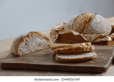 Rustic display of artisan bread on a wooden table. A whole loaf in a paper-lined tray with sliced pieces and a half loaf on a wooden board. Perfect for homemade baking and natural food themes.