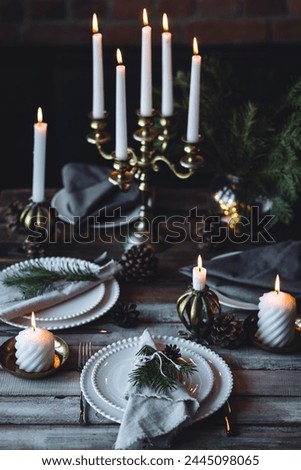 Rustic elegant table decor for christmas family dinner. Center piece with white candle, pine cone, fir tree branches. Zero waste eco-friendly home decoration. Cozy atmosphere, wooden background.