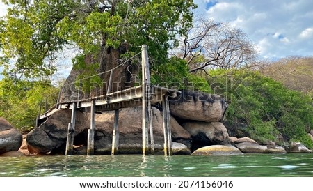 A rustic elevated jetty or pier next to a dramatic rockscape and tree on an island on Lake Malawi.