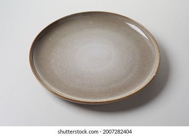 Rustic Empty Clean Mottled Brown Round Pottery Plate With Small Chip To The Rim On A White Studio Background In A High Angle View With Shadow For Food Advertising