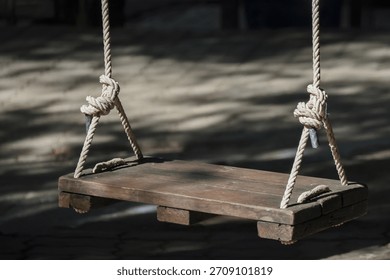 Rustic empty wood swing hanging from rope in an outdoor garden, evoking feeling of peaceful nostalgia. quiet and simple memory from childhood waiting for someone