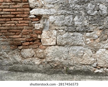 A rustic exterior wall shows a patchwork of exposed old brick and rough-hewn stone repairs, weathered by age and time.