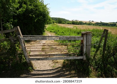 A rustic farm gate with a 'Keep Gates Shut' sign stands on a sunlit dirt path in Morton, Nottinghamshire, England. Golden fields and lush green trees stretch into the peaceful countryside.