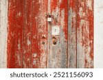 Rustic, flaking, peeling red pain on a rotting and decaying door with rusty lock and keyhole at an abandoned house’s doorway