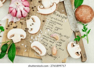 Rustic flat lay with fresh brown mushrooms, garlic, parsley, knife and handwritten recipe on white linen background, top view