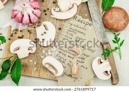Rustic flat lay with fresh brown mushrooms, garlic, parsley, knife and handwritten recipe on white linen background, top view