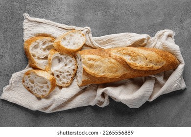 Rustic French sourdough baguette on a towel on a gray table, top view