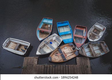 A rustic gathering of old worn empty, vintage rowboats clustered together over dark water at Dysart Harbour in Fife, Scotland.
