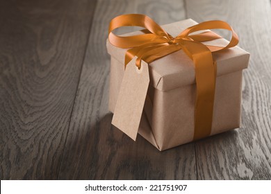 Rustic Gift Box With Orange Ribbon Bow And Empty Tag, On Old Wood Table