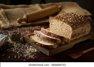 Rustic grain bread with oats, flax seeds, sunflower seeds and sesame seeds on a wooden board with a jute sack and a rolling pin on the background - Powered by Shutterstock