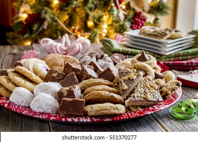 Rustic Holiday Party Table With Tray Of Homemade Cookies And Candy With Holiday Napkins And Plates In Front Of Christmas Tree