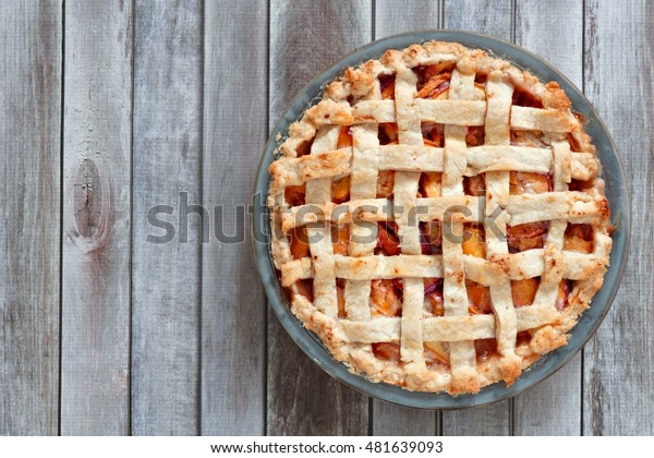 Rustic homemade peach pie in baking plate,\
above view on a wood\
background