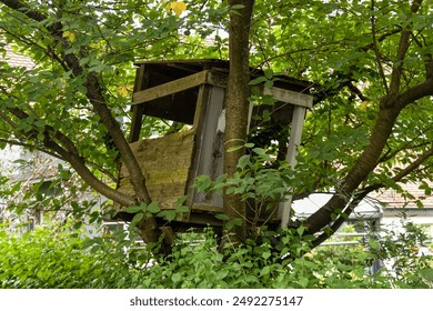 A rustic, homemade wooden treehouse built by children, nestled among lush green foliage. The simple structure is perched securely in the branches of a tree, creating a charming and nostalgic scene. - Powered by Shutterstock