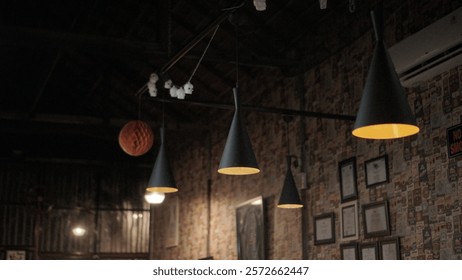  A rustic interior featuring several pendant lights with a modern design. The lights are predominantly black with warm yellow illumination. One light is orange and textured. 
