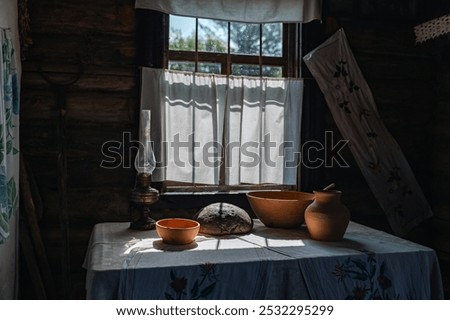 Rustic interior with a window bathed in sunlight. The room is dimly lit, but the window lets in a bright beam of light, highlighting a table set with a clay jug, a bowl.