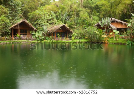 A rustic jungle hut in Ecuador's Amazon rainforest, surrounded by lush greenery, lianas and the flowing waters of the mighty Amazon River.