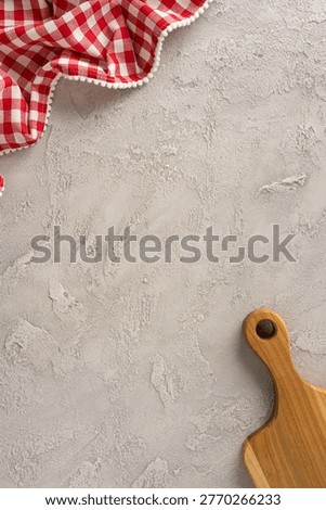 Rustic kitchen composition for cooking and preparation with red gingham cloth and wooden cuttingboard on a textured concrete background offering empty space for recipe styling