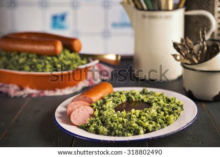 A rustic kitchen with a plate with 'Boerenkool met worst' or kale with smoked sausage, a traditional Dutch meal. Served with gravy. With typical Dutch Delft blue tiles on the wall in the background.