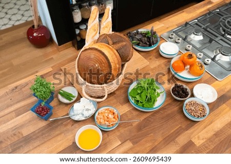 A rustic kitchen prep scene ready for brunch magic — with crusty artisan loaves, fresh greens, creamy cheeses, vibrant herbs, seasonal fruits, and a colorful mix of toppings all laid out.