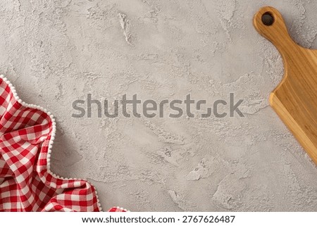 Rustic kitchen scene for cooking preparation with a wooden cuttingboard and red checkered tablecloth on a textured concrete surface