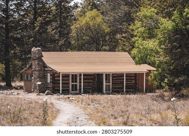 A rustic log cabin surrounded by trees in a serene forest setting, with a dirt path leading to the entrance.
