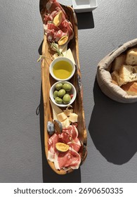 Rustic Mediterranean appetizer platter served in a wooden dish with prosciutto, cheese, figs, green olives, olive oil and freshly baked bread. Traditional antipasto captured in natural sunlight