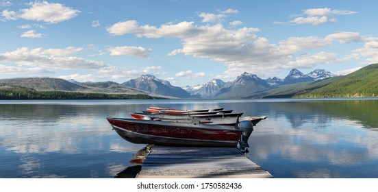 Rustic motor boats lined up in a perfect row on a wooden dock looking out onto Lake McDonald in the beautiful Glacier National Park, Montana 