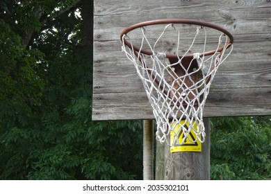 Rustic old basketball ring on a wooden shield on a summer day. Green trees foliage on the back. Wooden texture. Electricity sign under the shield.