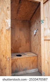 Rustic old interior view of an outhouse with no toilet seat and a roll of toilet paper hanging on the wall in the high mountains of the Nevada desert