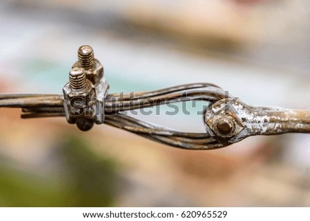 Rustic old steel cable loop, clamp, and bolts with faded, chipped paint against soft focus blurred background