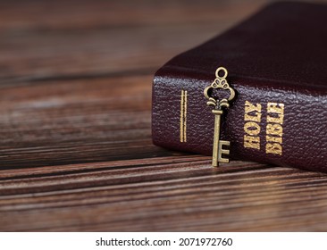A rustic old vintage retro key with closed Holy Bible book with gold text on a wooden table. A Christian biblical concept of revelation, prayer, faith, and trust in God Jesus Christ. A close-up. - Shutterstock ID 2071972760