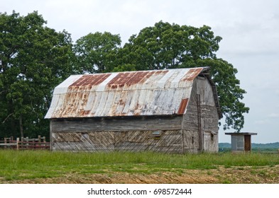 A Rustic Old Wooden Barn With A Peeling Tin Roof Looks Like A Piece Of Original Folk Art, With Its Slanted Timbers And Rusty Roof.