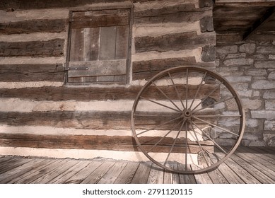 Rustic olf log cabin building exterior wall with an old wagon wheel leaned up against it.