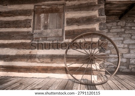 Rustic olf log cabin building exterior wall with an old wagon wheel leaned up against it.