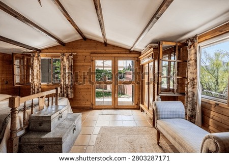Rustic open-plan living area with log cabin walls, terracotta tiles, large windows, and a loft staircase