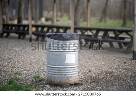 Rustic outdoor setting featuring a trash barrel at a picnic area.