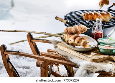 Rustic outdoor winter barbecue in snow with crusty twist bread on wooden skewers, dips and ketchup on a wooden table