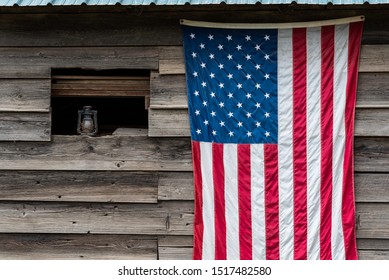 Rustic outside wall of wood building with green metal roof, open window with dusty lantern on windowsill, American flag hanging on wall
