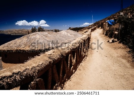 A rustic pathway winds through a traditional Bolivian village near Lake Titicaca. The thatched-roof huts and mud walls capture the essence of rural life in the Andes.