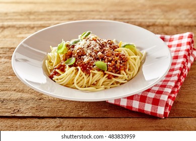 Rustic plate of tasty spaghetti Bolognaise topped with grated parmesan cheese and fresh basil served on a plate with a red and white checkered napkin