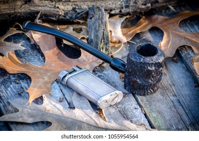 rustic popeye pipe, also called a setter pipe, on a rustic outdoor background with a antique silver flint lighter